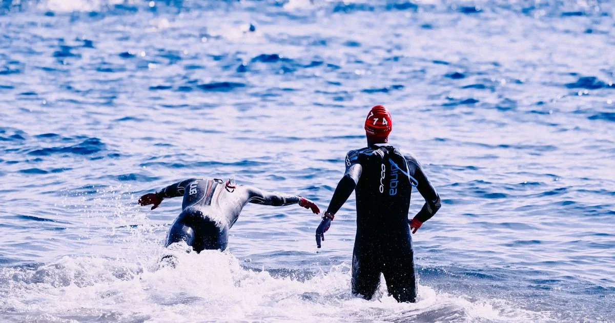 Triathlètes alignés au départ d'un triathlon en eau libre, bonnets colorés